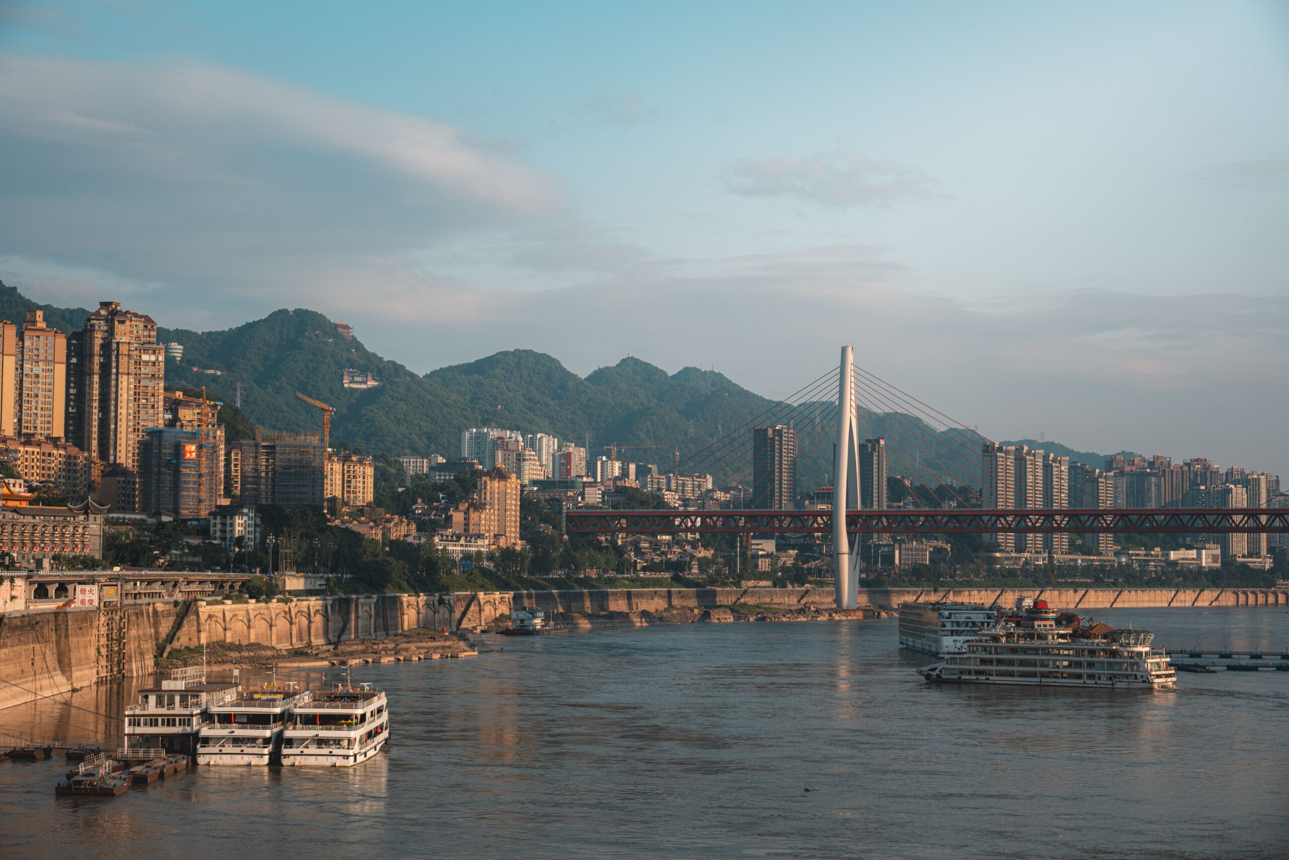The Chongqing riverfront with a bridge, city buildings and forested hills.