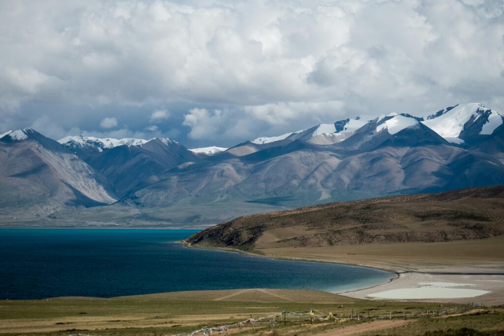 Deep blue alpine lake beneath snow-capped mountains and storm clouds in Qinghai