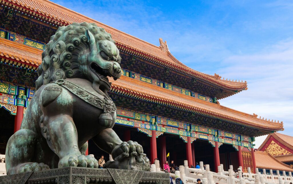 Bronze guardian lion and ornate imperial roofs at Beijing's Forbidden City