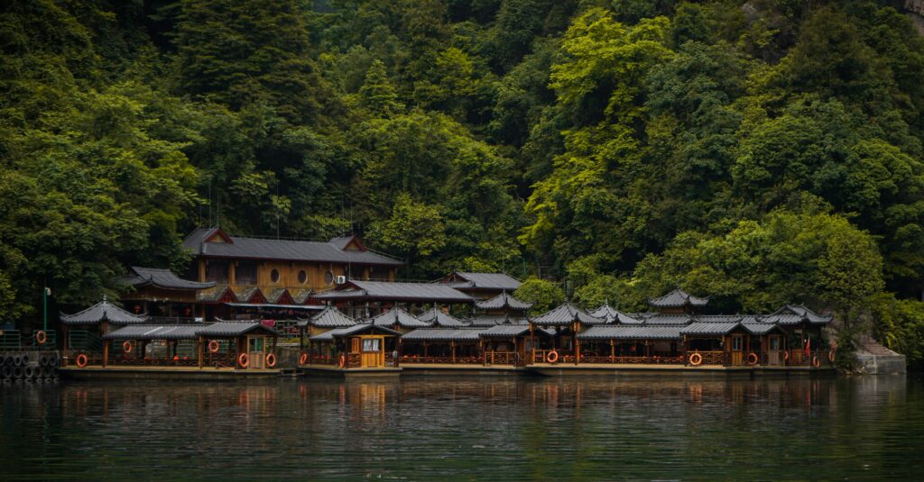 Traditional roofed boats and lakeside buildings on a forested lake in Zhangjiajie