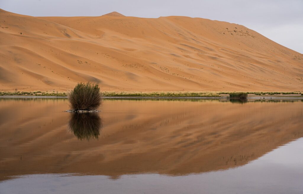 Sand dunes reflected in a calm desert lake in Badain Jaran Desert, China