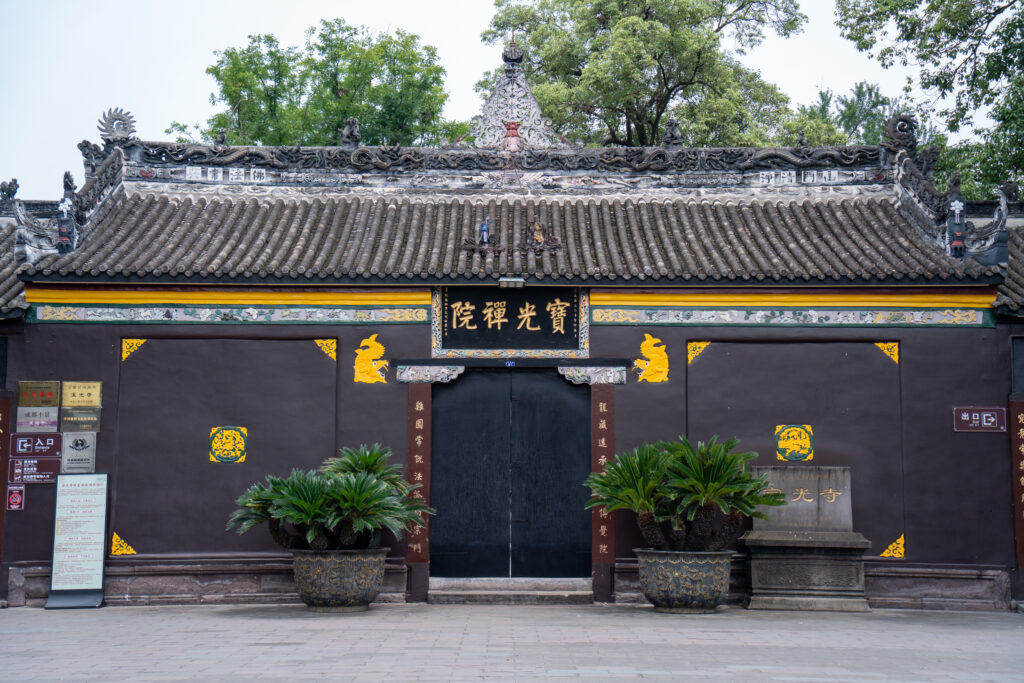Ornate tiled entrance gate at Baoguang Temple framed by leafy trees
