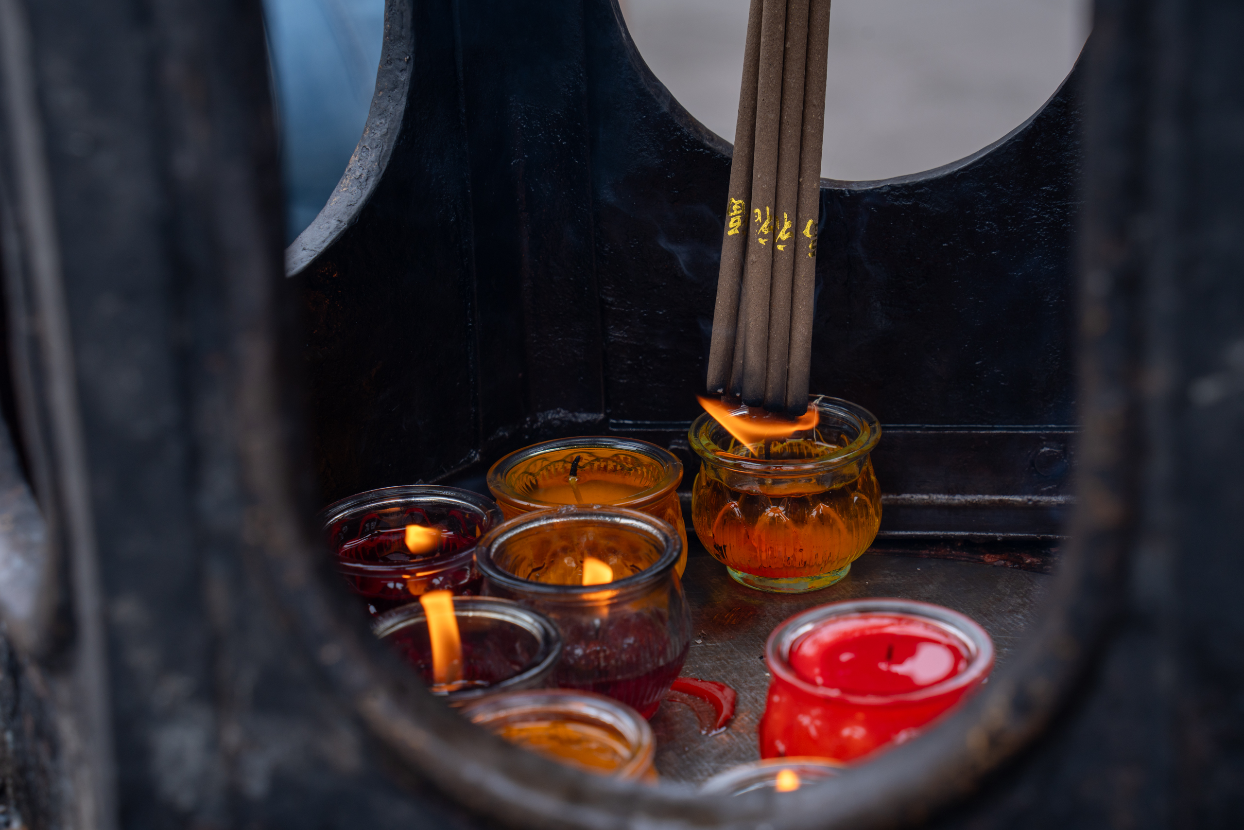 Burning incense sticks and small candles glow inside a temple burner