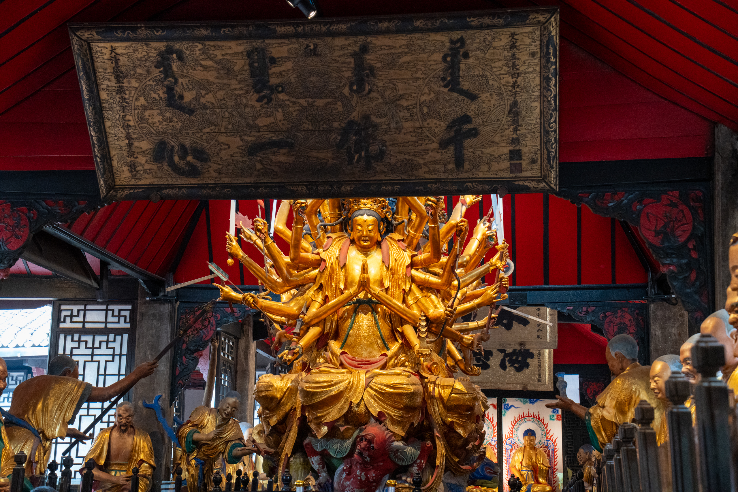 Gilded multi-armed Buddhist statue surrounded by carved figures inside Baoguang Temple